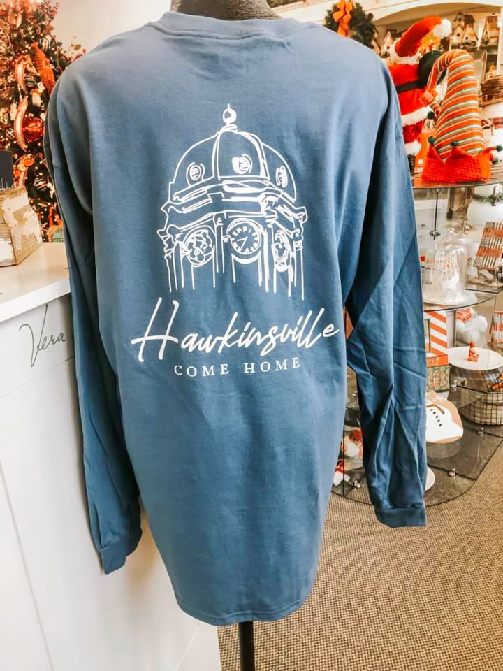 A blue t-shirt with the Hawkinsville, Come Home brand printed on the back.