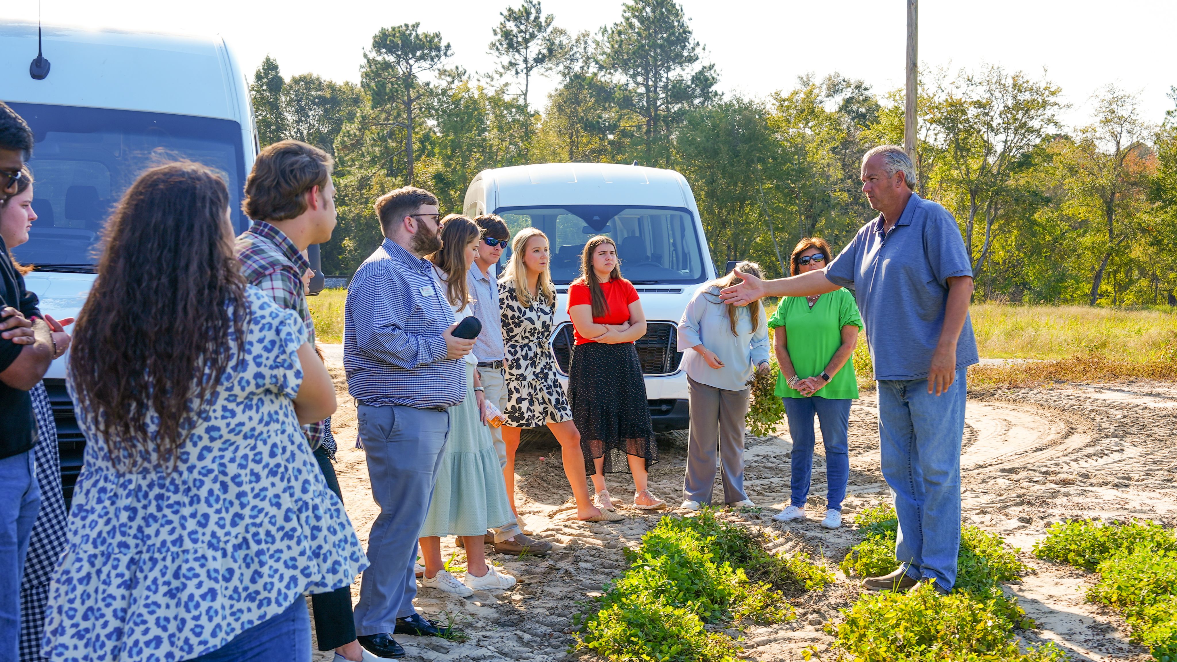 People standing next to peanut field with man gesturing 